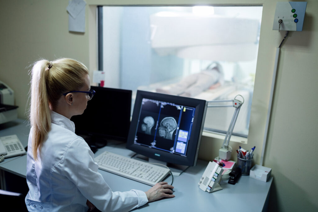 Female doctor analyzing digital brain scan results on computer monitor in the hospital.